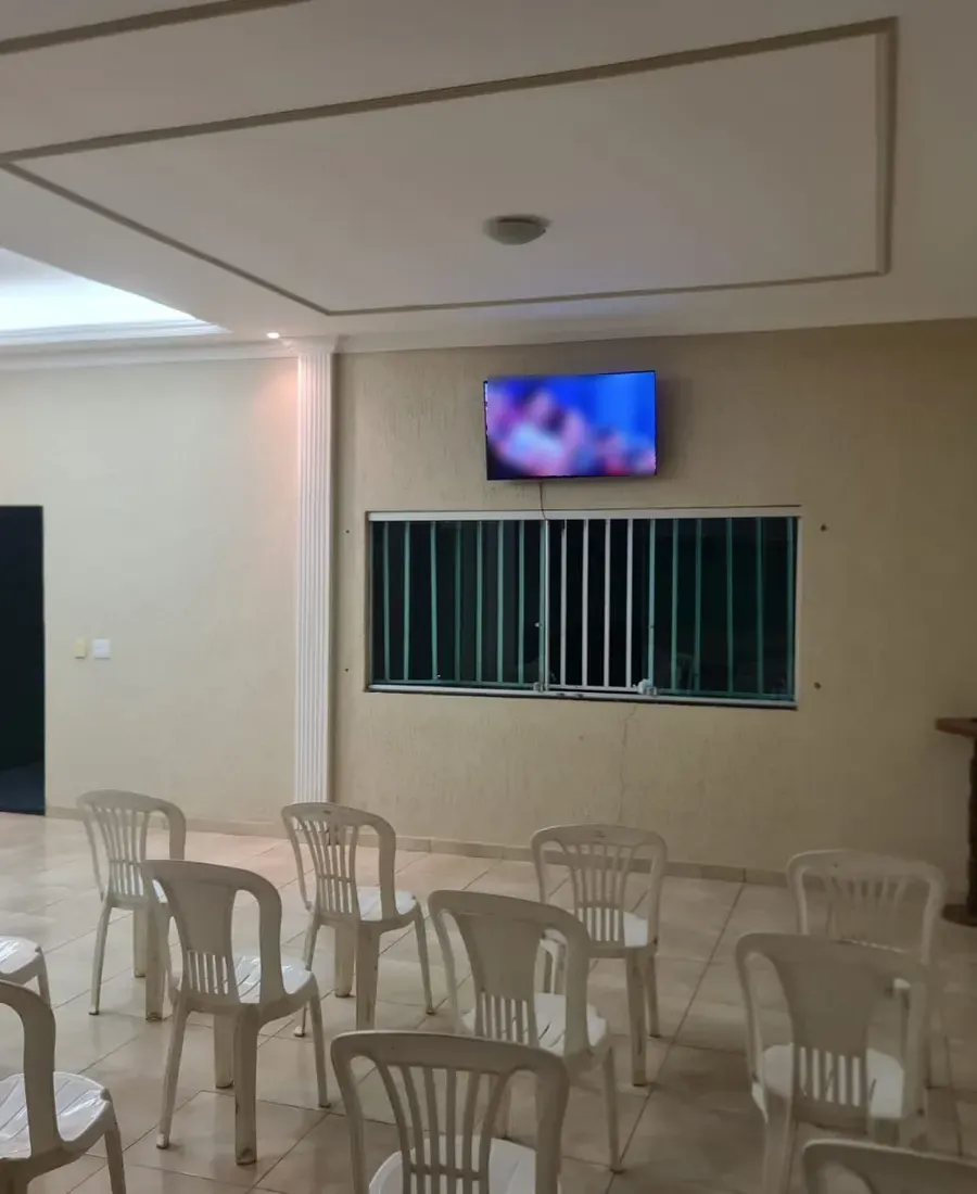 Sala de convivência com cadeiras de plástico enfileiradas de frente para a TV